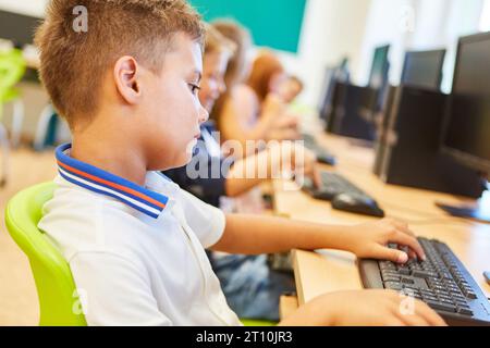 Side view of elementary schoolboy using computer while sitting on chair in class Stock Photo