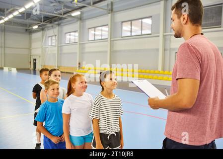 Male teacher taking physical test of elementary students standing in line during gym class Stock Photo