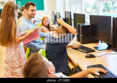 Male and female elementary students talking with teacher sitting in computer class Stock Photo