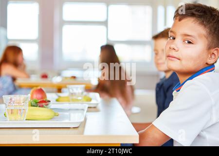 Side view portrait of boy sitting with fruits tray on table at cafeteria in school Stock Photo