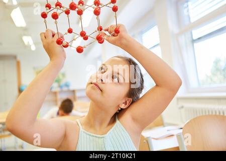 Curious schoolgirl examining molecular structure while sitting in classroom Stock Photo