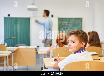 Portrait of smiling elementary male student sitting on bench during lecture in classroom Stock Photo