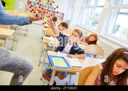 Smiling schoolkid touching molecular structure sitting on bench in classroom Stock Photo