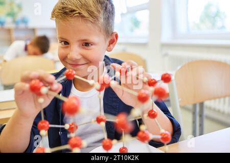 Smiling elementary schoolkid learning through molecular structure in class Stock Photo
