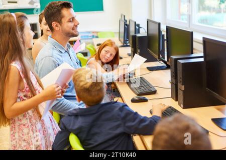 Smiling teacher sitting with male and female elementary students in computer class Stock Photo