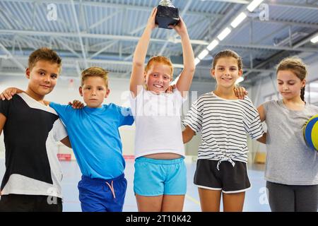 Portrait of happy schoolgirl holding trophy with friends standing in school gym Stock Photo