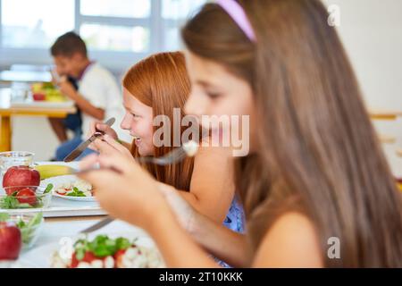 Happy girl having meal with friend during lunch time in school cafeteria Stock Photo