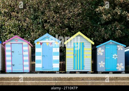 A row of four brightly painted individual wooden beach huts at the back of a beach in the isle of wight, UK Stock Photo