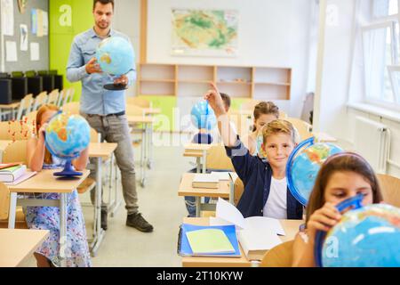 Male and female students studying with globes with teacher in classroom Stock Photo