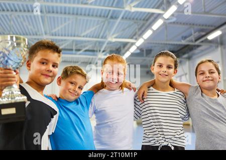 Portrait of smiling male and female students holding trophy while standing in school gym Stock Photo