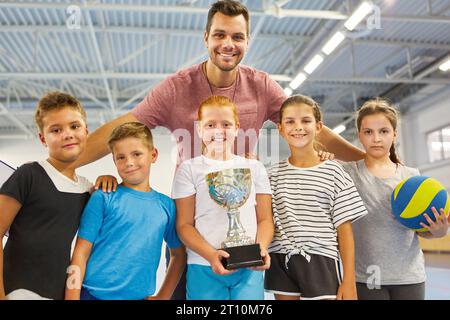 Portrait of smiling male teacher with students holding trophy while standing in school gym Stock Photo