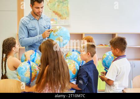 Male teacher explaining maps through globe to elementary students in class Stock Photo