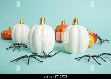 set of Small ceramic pumpkins in different colors among an invasion of spiders on a turquoise background. Minimalist, trendy still life photography in Stock Photo