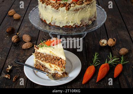 Carrot cake with walnuts on a dark wooden background. Selective focus. A piece of cake in a dish and walnuts and carrots arround. Stock Photo