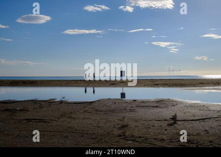 People strolling along the seashore, clear day, blue tones, beach sand, reflections Stock Photo