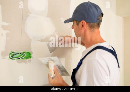 Professional home painter repairing holes and cracks with plaster. Stock Photo
