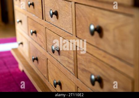 Cabinet of small drawers all closed. Wooden drawers with metal pull knobs. Selective focus on the second row of drawers. Storage in neat compartments Stock Photo