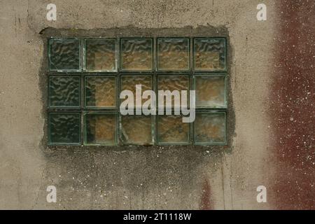 Old wall with glass block window. Translucent square glass tiles. Rough ribbed surface of green glass of window. Vintage texture for background and de Stock Photo