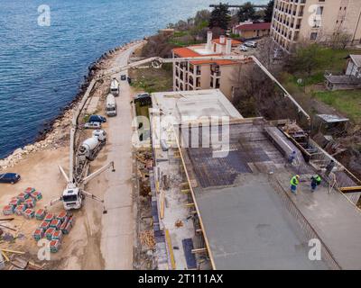 Pouring concrete cement on the roof of residential building under construction using a concrete pump truck machine with high boom to supply the mixtur Stock Photo