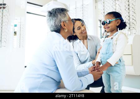 Optometrist, mother and child holding hands shopping for spectacles in trial frame at store. Mature ophthalmologist, mom and happy kid in test for Stock Photo