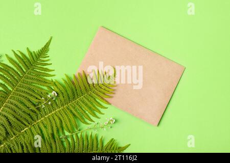 Light brown craft envelope and fern leaves on green background. Invitation to the holidays. Flat lay. Stock Photo