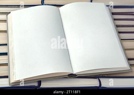 An open book with blank pages, a diary on a stack of old books standing upside down. Mock up for text Stock Photo