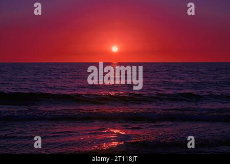 The blood red sun sets on the blue ocean. Dramatic sunset on the sea Stock Photo
