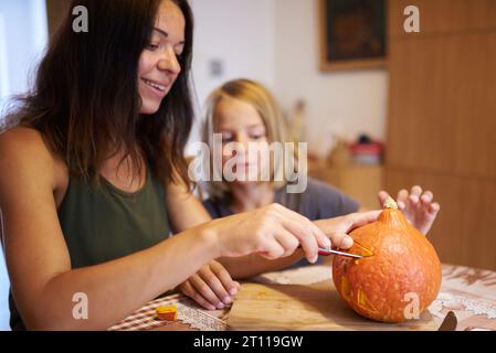 Happy family preparing for Halloween. Mother and boy carving pumpkin at home. Stock Photo