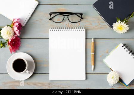Top view of the desktop. Spiral notebook with an open blank page, glasses, pen, white cup with black coffee, dahlia flowers. Festive office desktop co Stock Photo