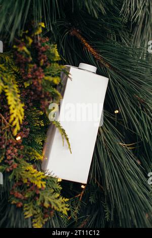 A paper bag of milk on a Christmas background of pine branches. Mockup for logo design. Stock Photo