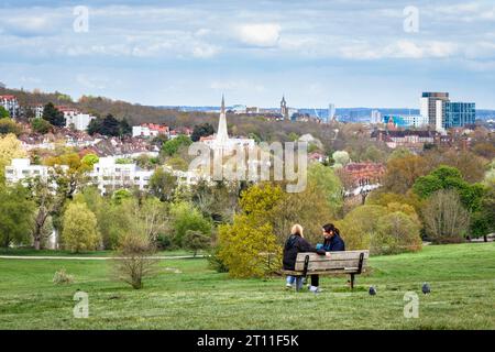 View north-east across London from Parliament Hill on Hampstead Heath, two women chatting on a bench in the foreground, London, UK Stock Photo