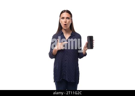 a young woman with black hair dressed in a blue blouse with surprise shows a smartphone with a mockup Stock Photo