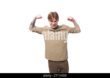 a young slender red-haired caucasian guy dressed in a khaki short-sleeve shirt shows muscles Stock Photo