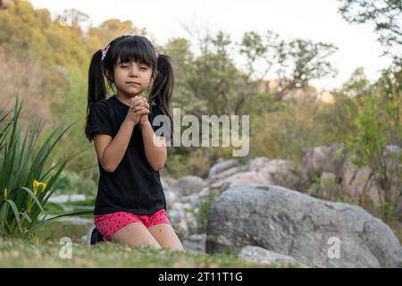 Little girl praying in a natural environment. Stock Photo