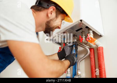 Closeup of plumber using screwdriver while fixing boiler or water heater, working on heating system in apartment Stock Photo