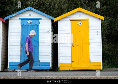 A man walks past two brightly coloured individual wooden beach huts located off a beach in the Isle of wight, UK. Stock Photo