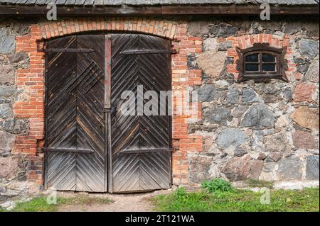 Small figured window and a large closed wooden gate leading into the stone barn. From the series Doors of the World. Stock Photo