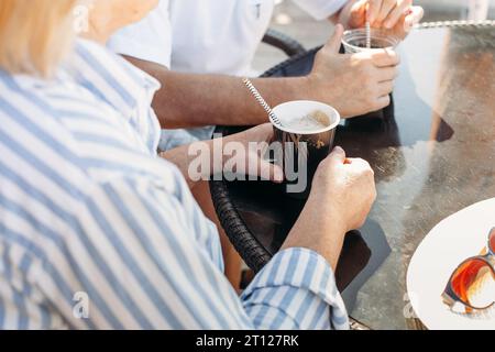 An elderly couple, a man and a woman, are drinking frappuccino and cappuccino. Close-up of hands and coffee drinks. Stock Photo