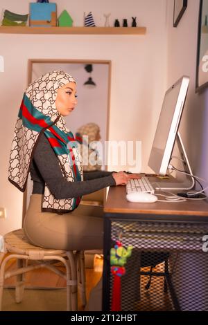 Veiled Arab girl at home computer, working from home. Modern Arab young woman with new technologies Stock Photo