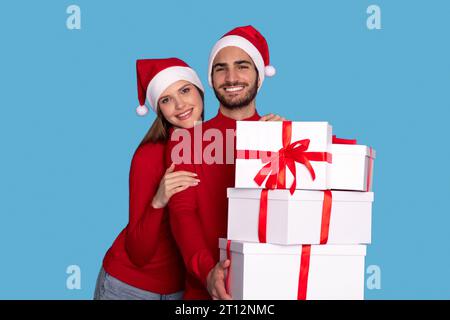 Happy Young Couple Holding Stack Of Christmas Presents And Smiling At Camera Stock Photo