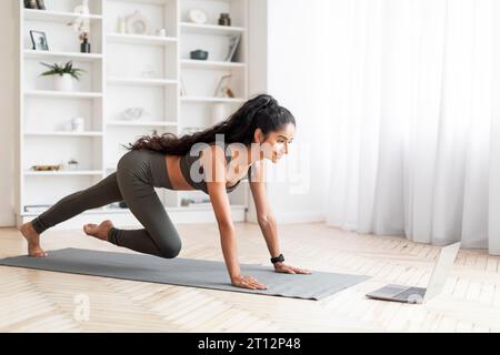 Active Millennial Indian Woman Undertaking Digital Exercise Session, Home Interior Stock Photo