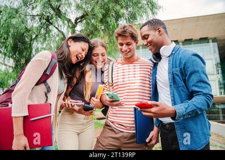 Group of students having fun together sharing on the social media with a cellphone app. Happy friends using their smartphones. Multiracial teenagers browsing on internet with a mobile phone at campus. High quality photo Stock Photo