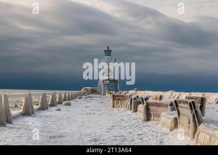 thick Ice formations over the guard rails in the pier. and benches, Winter  landscape on the lake with lighthouse and stormy sky, winter wonderland Stock Photo