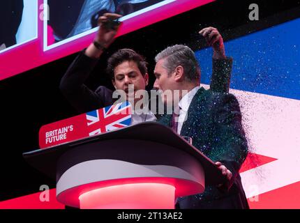 Protester covers  Keir Starmer with glitter during the start of the leaders speech.The protester was wrestled to ground and removed by security. Sir Keir Brushed his hair removed his jacket and carried on with speech. Labour Conference 2023. Picture: garyroberts/worldwidefeatures.com Stock Photo