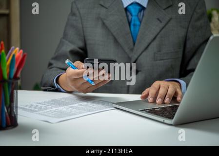 man using smartphone mobile application and document information with laptop on desk. Stock Photo