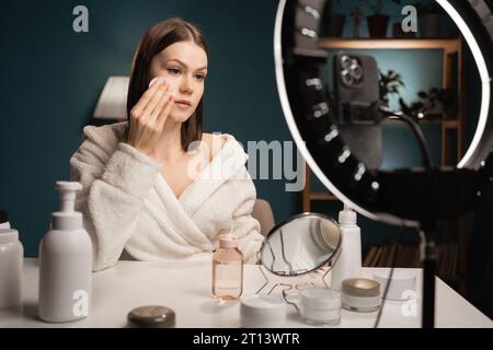 Woman cleaning face with white cosmetic cotton pad Removing Makeup, beauty blogger recording vlog on camera. Copy space Stock Photo