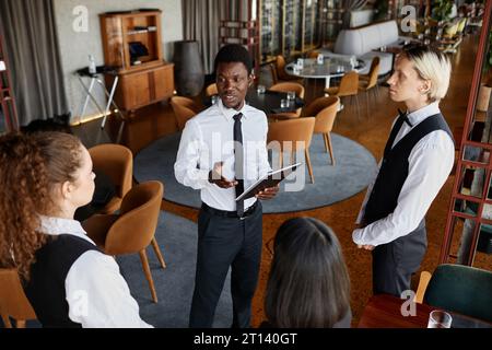 High angle portrait of restaurant manager talking to servers wearing classic uniforms during staff meeting in modern dining room Stock Photo