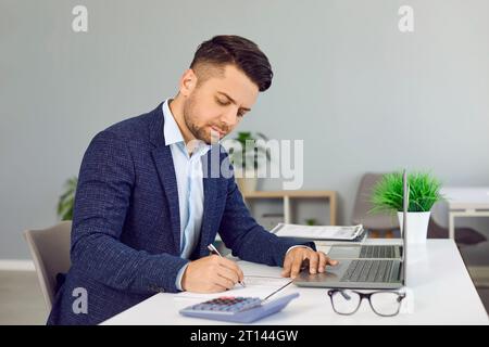 Serious businessman uses calculator to calculate business data while working at workplace. Stock Photo