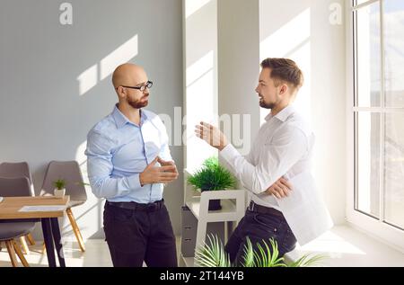 Two focused male colleagues talking while standing in modern office Stock Photo