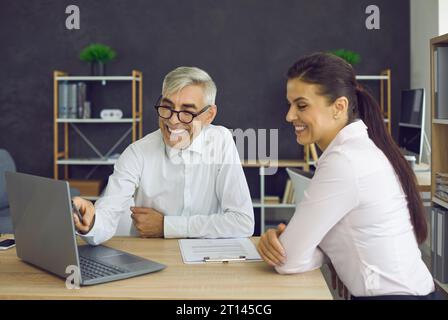 Smiling senior boss and young employee looking at laptop screen in office Stock Photo